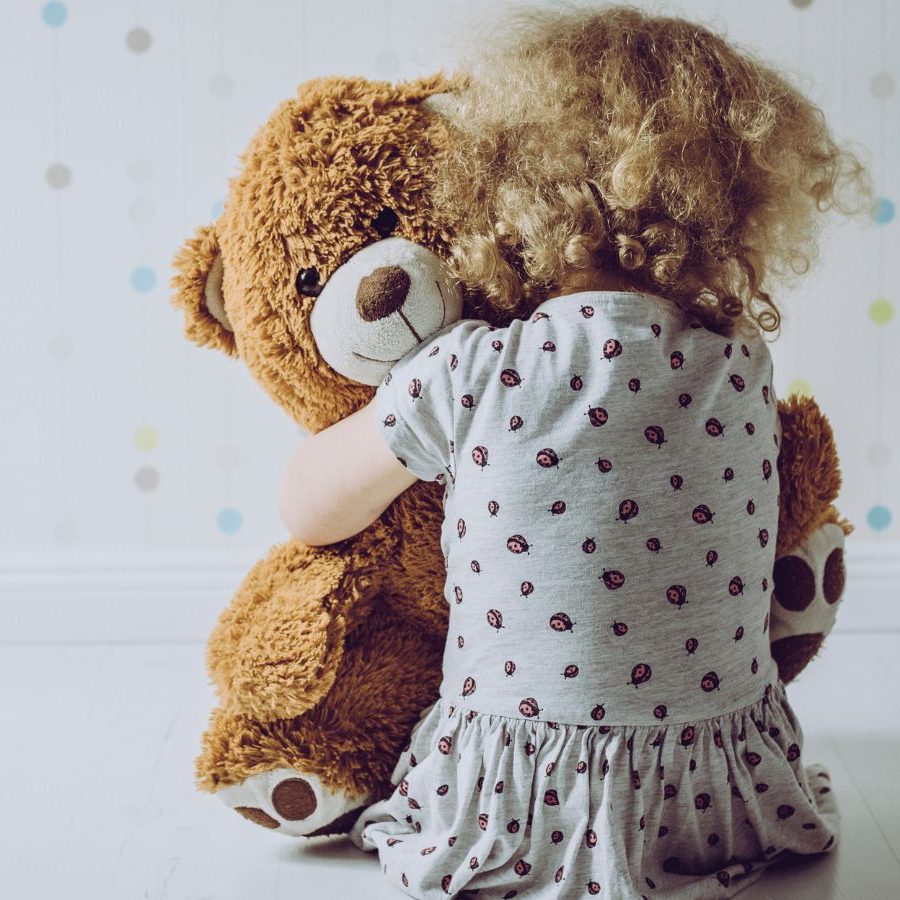 Child hugging a teddy bear with their back to the camera