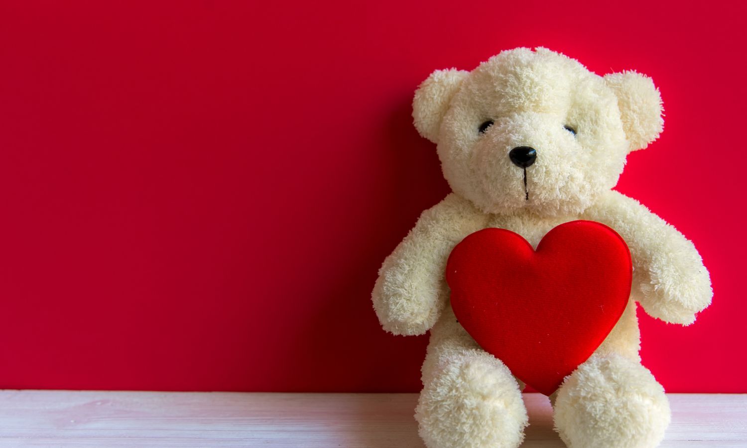 Teddy bear holding a heart and sitting against a red background