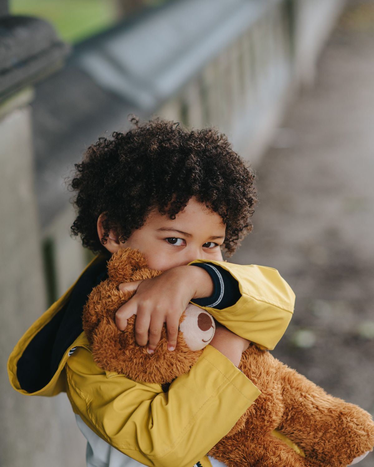 Child in yellow jacket hugging a teddy bear.